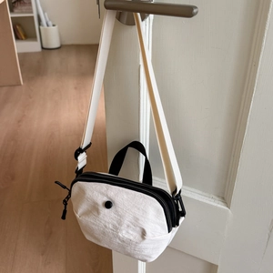 Detail of a minimalist cream canvas crescent bag with black zipper and top handle hooks