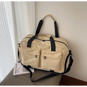 Detail of beige travel bag with large front pockets and black webbing handles on leather seat