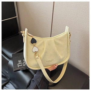 Détail du sac seau crème avec plis verticaux et breloque double cœur sur la bandoulière