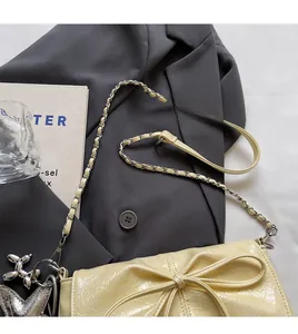 Detail of cream yellow bow shoulder bag with pleats and silver chain on grey blazer