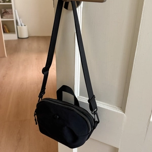 Detail of a compact black nylon crossbody bag with dual zippers and adjustable strap