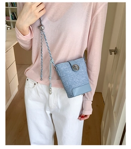 Detail of light blue bucket bag with metal lock and chain strap on a pink sweater