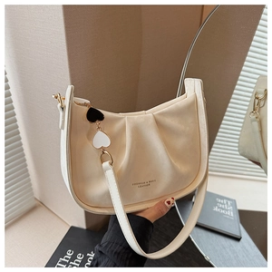 Détail du sac seau plissé beige avec logo doré et pendentif en forme de cœur élégant