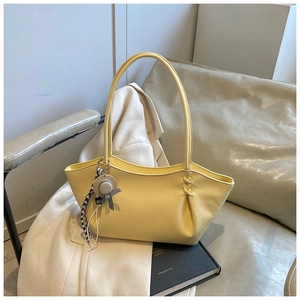 Detail of yellow tote bag with textured leather, unique folds, and straw hat pendant