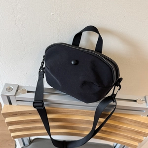 Detail view of the black canvas shoulder bag with double zippers and nylon strap on a chair