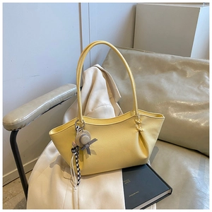 Detail of light yellow lychee grain leather tote bag featuring a straw hat charm