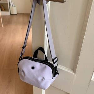 Detail of light purple nylon crossbody bag hanging on a door handle in a home setting