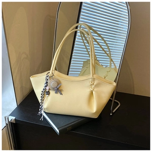 Detail view of beige tote bag featuring textured leather, cross stitching and cute charm