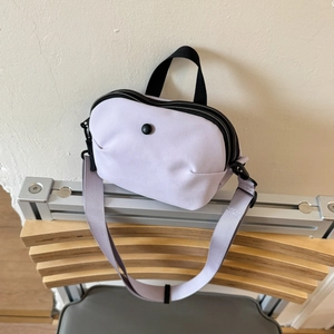 Detail view of light purple canvas crossbody bag on a stand with dual black zippers