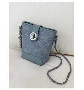 Detailed close-up of blue denim bucket bag with silver rotary lock and chain strap