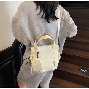 Detail of a creamy white nylon bucket bag with a small round coin purse charm and strap