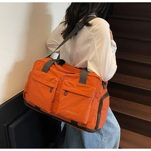 Close-up of orange travel bag with multiple zipper pockets and wide black strap