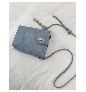 Detail of grey-blue denim texture bucket bag with silver lock and skull charm
