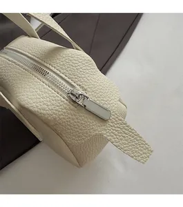Gros plan détaillé sur la fermeture éclair argentée et le cuir grainé du sac à main crème