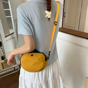 Detail of yellow canvas crossbody bag with adjustable strap worn by a model in casual style