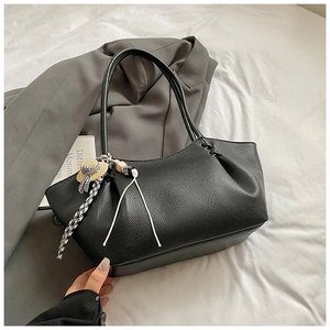 Detail of black pebbled leather tote bag with curved rim and mini straw hat charm