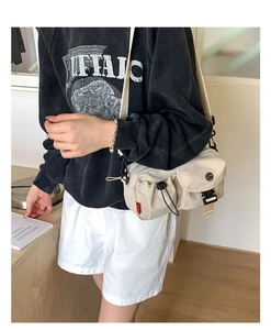 Detail of off-white crossbody bag with utilitarian buckles and drawstring side pocket