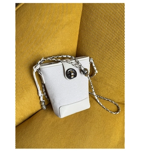 Detail of white tweed bucket bag with silver chain strap and metal swivel lock on yellow sofa