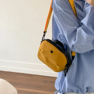 Detail of yellow canvas crossbody bag with orange strap and black zipper closure