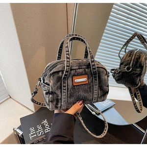 Detail of grey washed denim mini Boston bag with orange leather patch and metal tag