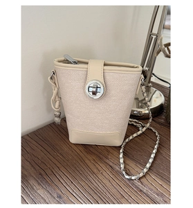 Detail of cream bucket bag showing woven texture, silver twist lock and peanut charm