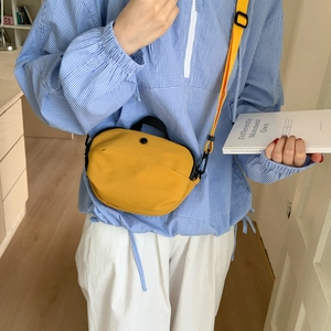 Detail of yellow canvas crossbody bag with black handle worn with casual shirt