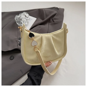 Détail du sac bandoulière en cuir crème avec design plissé et breloque cœur