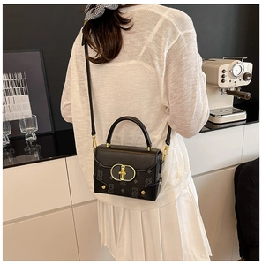 Detalle del bolso bandolera negro con estampado de oso y hebilla dorada en un café acogedor