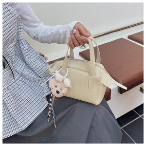 Détail d'un sac à main en cuir texturé crème avec un charmant porte-clés ours en peluche