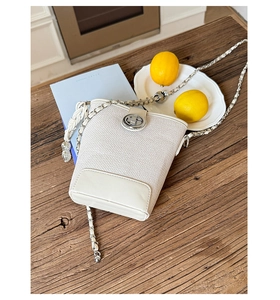 Detail view of white bucket bag with silver metal turn-lock and leather chain strap