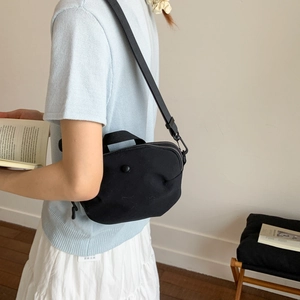 Detail of a minimalist black canvas crossbody bag featuring adjustable straps and round snap