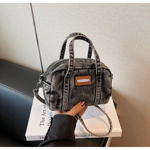 Close-up of black washed denim mini bowling bag with leather detail and adjustable strap