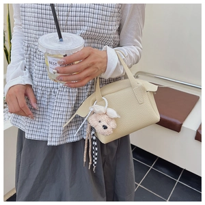 Détail d'un mini sac à main beige en cuir grainé avec un pendentif chien en peluche doux