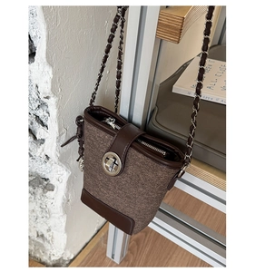 Detail of a brown bucket bag with textured fabric, leather accents, and silver chain strap