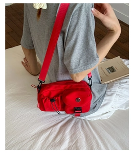 Detail of red multi-pocket nylon crossbody bag with drawstring and buckle closure