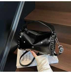 Close-up of black glossy barrel bag with heart studs and ruffles on wooden stairs