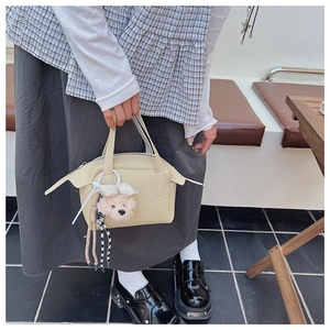 Détail du sac à main beige texture litchi avec breloque ours et décoration en corde