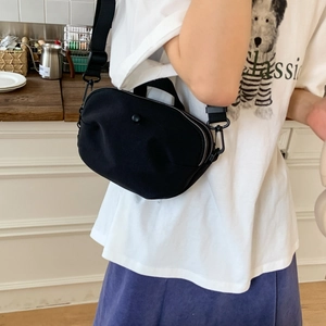 Detail of a black half-moon canvas crossbody bag with metal zipper and wide nylon strap