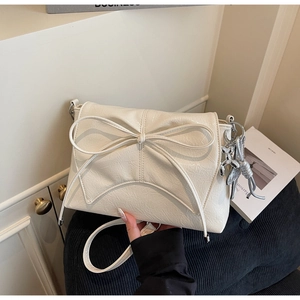 Détail du sac plissé blanc crème avec grand nœud et breloque chien ballon argentée