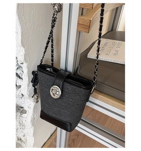 Detail of grey canvas bucket bag with black leather trim and silver twist-lock closure