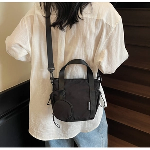 Detail of black nylon bucket bag with detachable round pouch worn by a model on stairs