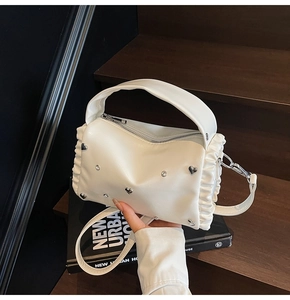 Detail of white tote bag featuring heart rivets and elegant side ruffle pleats