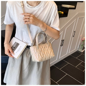 Close-up of pearl beige quilted crossbody bag with rhinestone accents on a model