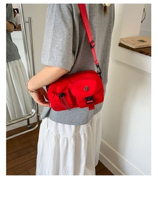 Detail of red nylon crossbody bag showing front flap pocket with buckle and side drawstrings
