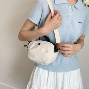 Detailed view of cream canvas crossbody bag with pleated texture and contrast strap