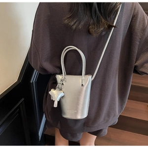 Silver bucket bag with star charm worn as a crossbody bag by a female model