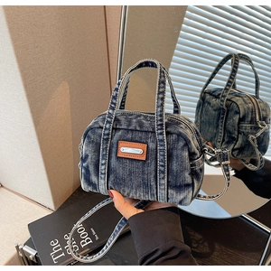 Detail of vintage blue denim handbag featuring leather logo patch and dual zipper design