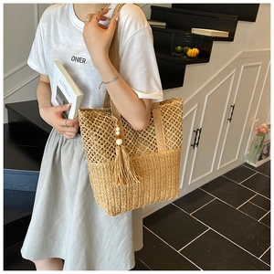 Detail of hollow woven straw tote bag with tassel wooden beads and shoulder strap