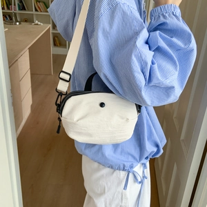 Close-up of white canvas crossbody bag featuring black zippers and woven shoulder strap