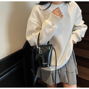 Detail of black glossy bucket bag featuring leather texture and doll charm on model